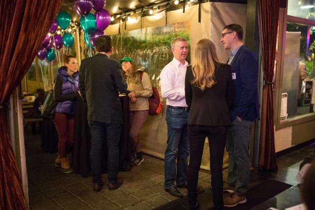 Group of attendees engaged in conversation at the Love Bomb 2017 event, decorated with purple and teal balloons, highlighting community support for My Voice Music nonprofit.